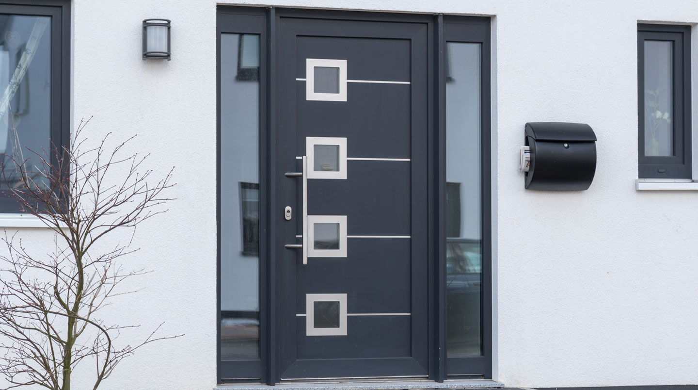 Un propriétaire en vêtements décontractés vérifie la température au niveau du cadre de sa porte d'entrée avec un appareil de mesure thermique