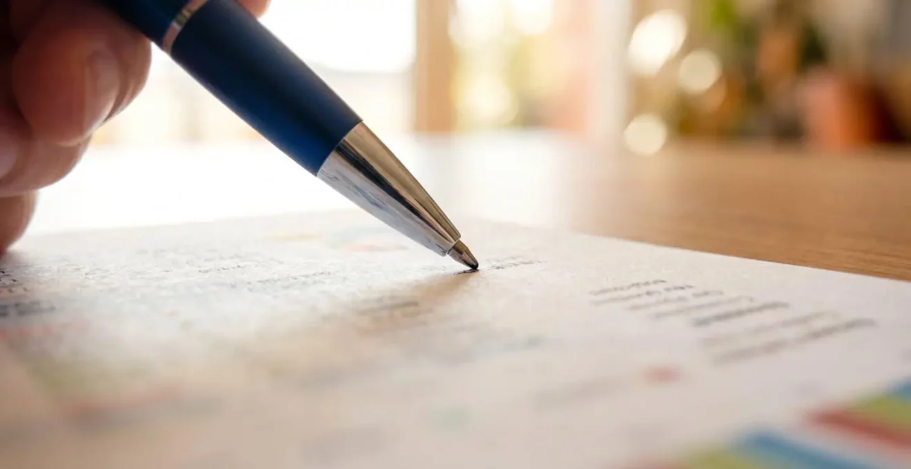 Gros plan d'une main tenant un stylo au-dessus d'un document de relance avec texte totalement flouté, arrière-plan en bokeh suggérant un bureau moderne